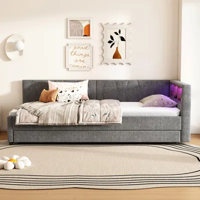 A daybed with bedding and decorative pillows in a room setting, with artwork on the wall and a rug on the floor.