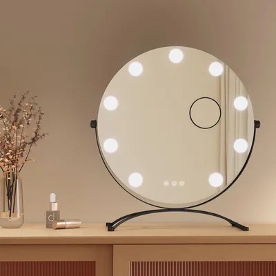 A makeup mirror with lights on a wooden dresser.