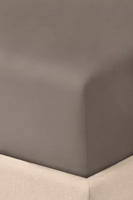 A close-up view of a fitted sheet on a bed, showing the corner and the texture of the fabric.