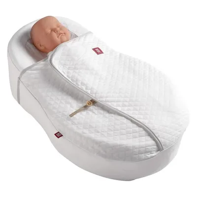 A baby doll is lying in a white baby cocoon or sleeping bag.