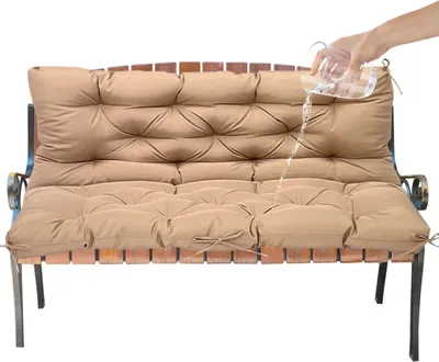 A hand is pouring water onto a taupe bench cushion to demonstrate its water-repellent properties.