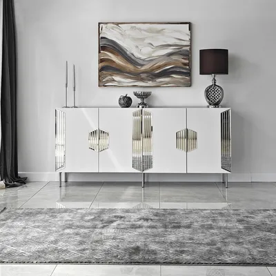 A white sideboard with silver decorative elements is displayed in a modern living room setting.