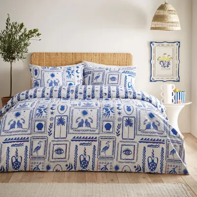 A bedroom scene with a bed dressed in a blue and white patterned duvet cover and pillows.