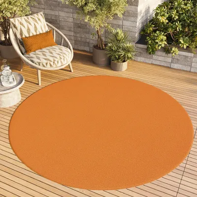 An orange circular rug on a wooden deck with a chair and plants.