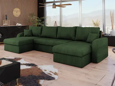 A spacious living room with a large green sectional sofa, a cowhide rug, and a black coffee table, featuring a large window with a view of mountains.