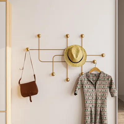 A gold coat rack mounted on a white wall, holding a straw hat, a brown purse, and a patterned dress on a hanger.