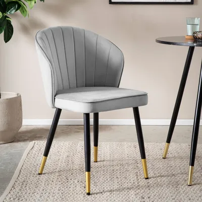 A gray velvet dining chair with black and gold legs is shown in a room setting.