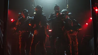 A group of soldiers in tactical gear standing in a dimly lit environment with red lights.