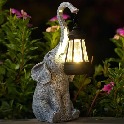 A solar-powered elephant statue holding a lantern in a garden setting at dusk.
