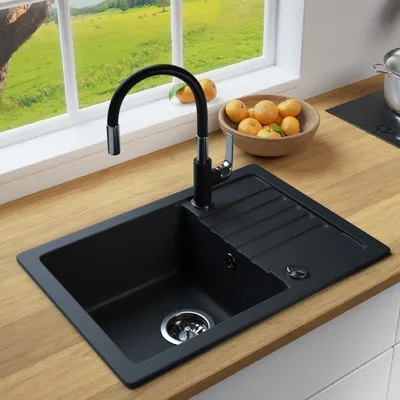 A black granite kitchen sink with a black faucet is shown on a wooden countertop, with a window view of a green landscape and a bowl of oranges in the background.