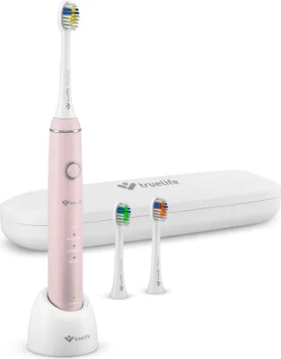 A pink electric toothbrush with its charging base and two replacement brush heads, displayed on a white background with a white carrying case in the background.