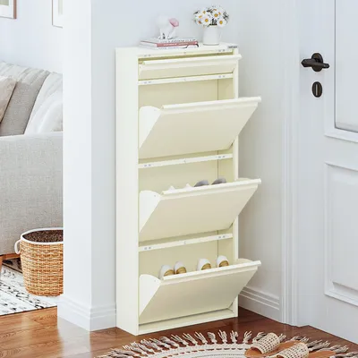 A cream-colored shoe rack with multiple flip-down compartments is shown in a hallway next to a door and a sofa.