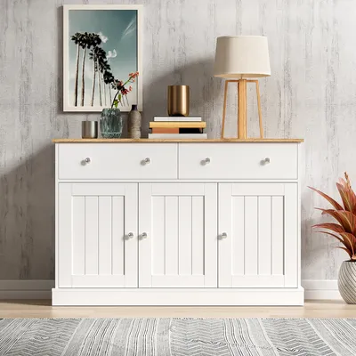 A white sideboard with wooden top, decorated with a framed picture, books, and a lamp.