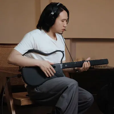 A person is playing a smart guitar while wearing headphones.