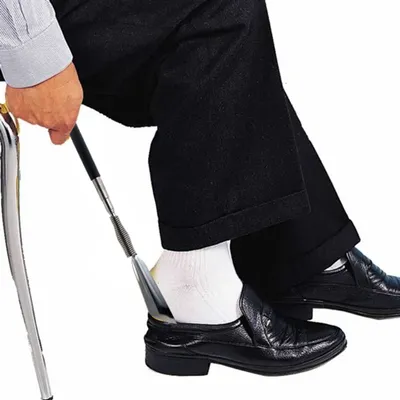 A person is using a shoehorn to put on a black shoe.
