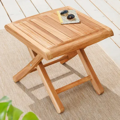 A wooden side table on a rug with a wooden deck in the background.