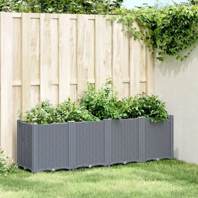A grey planter box filled with green plants sits on a lawn in front of a wooden fence.