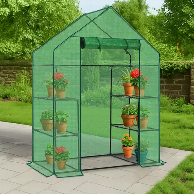 A green greenhouse with plants on shelves, set up on a patio in a garden.