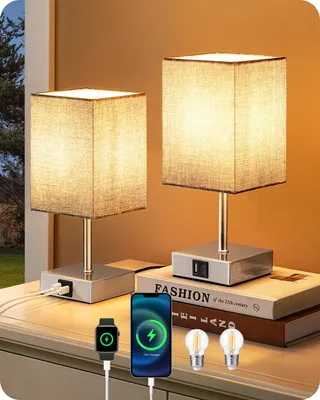 Two bedside lamps with USB charging ports are displayed on a nightstand next to books, a smartphone, and a smartwatch.