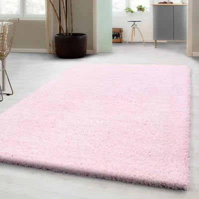 A pink shaggy rug is laid out on a light gray floor in a room with natural light coming from windows.