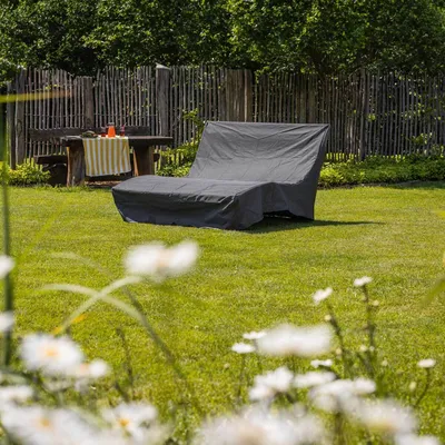 A covered chaise lounge in a grassy backyard with a wooden fence and a table with drinks.