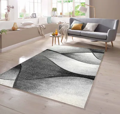 A modern living room with a grey sofa, a small side table, and a rug with a wave-like design.