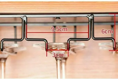 A close-up shot of a black metal wine glass rack mounted under a wooden surface, with wine glasses hanging from it. Dimensions are indicated with red lines and text.