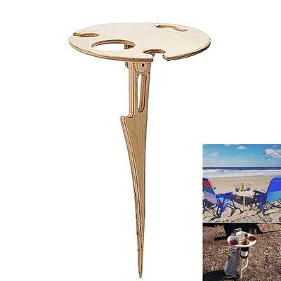 A wooden outdoor table with a pointed base for insertion into the ground, designed to hold wine glasses and bottles. The table has cutouts for wine glasses and a central area for a bottle or other items. The image also includes a smaller inset image showin