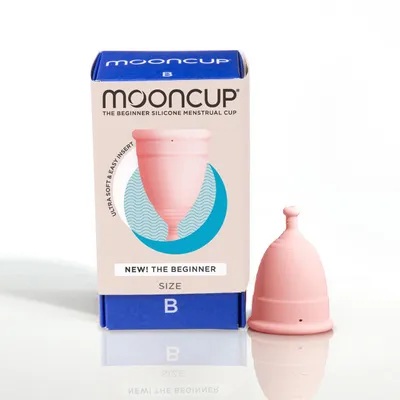 A mooncup beginner menstrual cup size B up side down with the packaging box on its left.