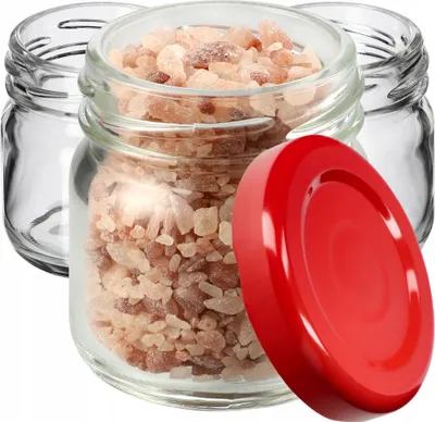 Three small glass jars, one filled with pinkish crystals, and a red lid are arranged on a white background.