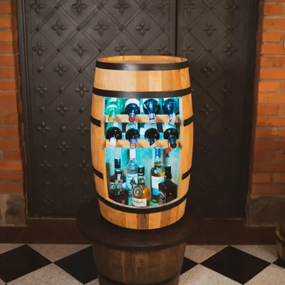 A wooden barrel wine bar with bottles of alcohol displayed inside, set against a dark, ornate door and brick wall.