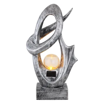 A silver abstract sculpture with a crackled glass orb illuminated by a warm light, set against a white background.