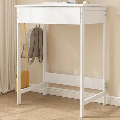 A white desk with a backpack and purse hanging on it, set against a light beige wall and wooden floor.