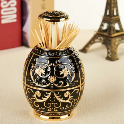 A decorative black and gold toothpick holder is shown on a table with books and a miniature Eiffel Tower in the background.