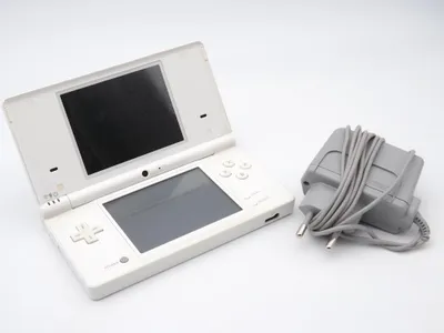 A white Nintendo DSi handheld game console and its gray charger are placed on a white background.