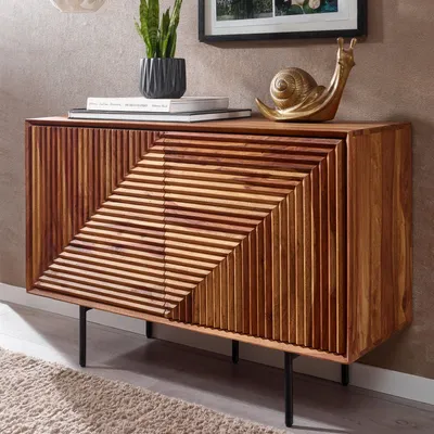 A wooden sideboard with a slatted front design, placed in a room setting with a rug and a plant on top.