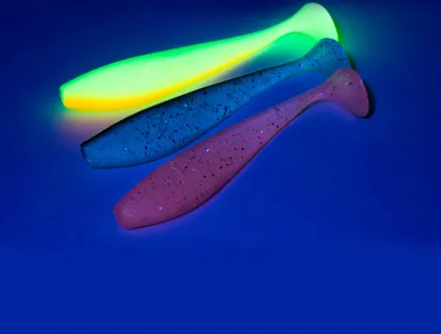 Three fishing lures are arranged diagonally on a blue surface, with the top lure glowing green and yellow under UV light.