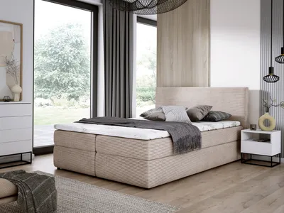 A bedroom scene featuring a beige boxspring bed with a mattress and topper, set against large windows and modern decor.