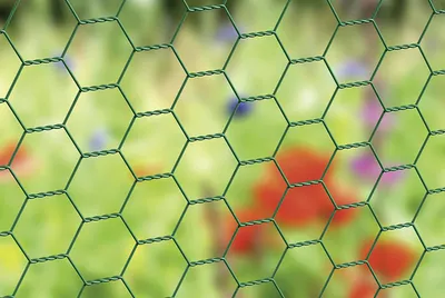 A close-up view of green hexagonal wire mesh, with a blurred background of flowers and greenery.