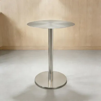A stainless steel bar table with a round top and base, set against a light wood paneled wall and a concrete floor.