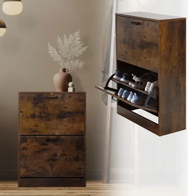 A shoe cabinet with two flip-out drawers is shown in a room setting, with a vase and plant on top of a similar cabinet to the left. The shoe cabinet is open, displaying shoes inside.