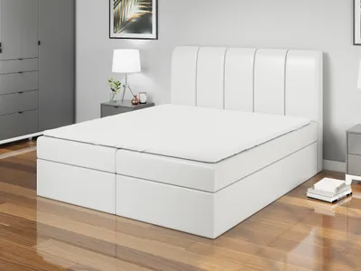 A white boxspring bed with a headboard is shown in a bedroom setting.