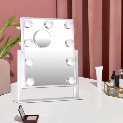 A makeup mirror with lights is placed on a white surface, with a pink curtain in the background.