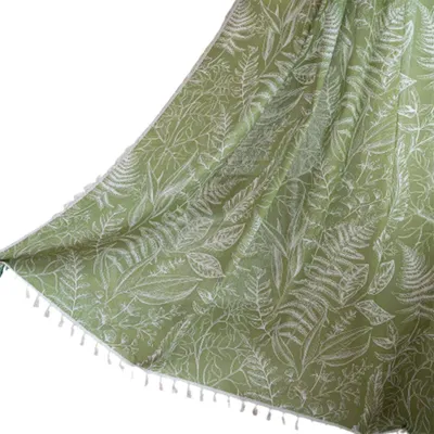 A close-up view of a green fabric with a white fern pattern and tassels along the bottom edge.