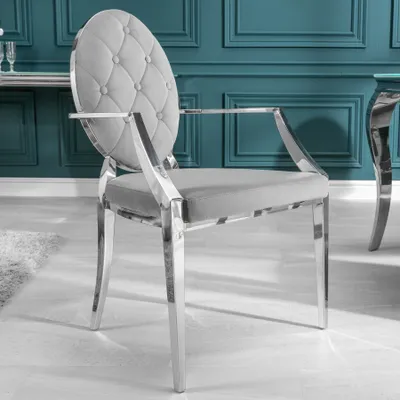 A close-up studio shot of a single grey velvet armchair with silver metal legs and frame, set against a teal wall.