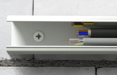 Close-up view of electrical and coaxial cables inside a white cable management channel mounted on a brick wall.