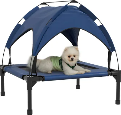 A small white dog wearing a green vest is lying on a raised blue dog bed with a blue canopy.