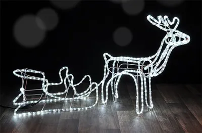 A lighted reindeer and sleigh decoration on a wooden floor against a dark background.