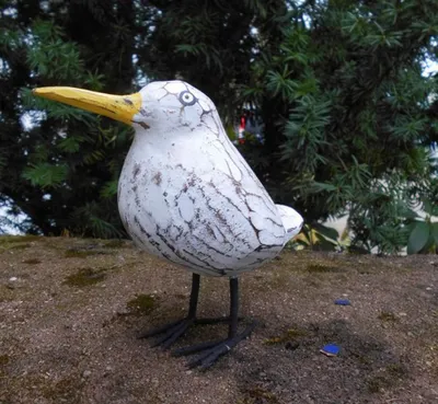 A decorative wooden bird figurine standing on a textured surface with greenery in the background.