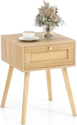 A light wood nightstand with a rattan drawer front, a cup of coffee, and a vase of dried flowers on top, set against a white background.